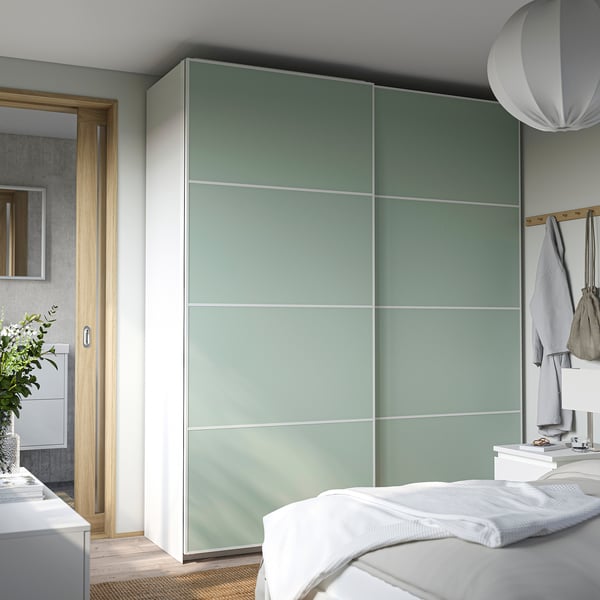 Modern bedroom tall light green PAX wardrobe. Its sleek design and size dominate the room, holding ample storage with a clean, minimalist appeal.