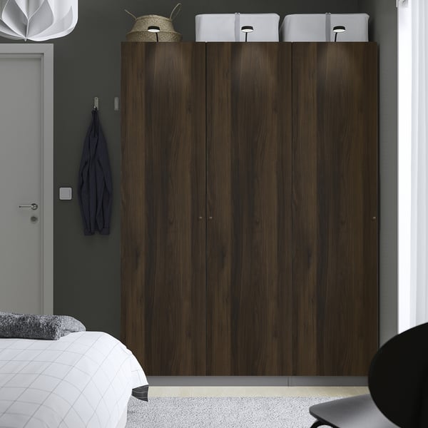 Modern bedroom with large dark brown PAX wardrobe, white boxes, blue sweater, bed with white headboard.