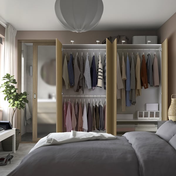 Bedroom with open wardrobe displaying clothes, featuring integrated lighting and adjustable feet.