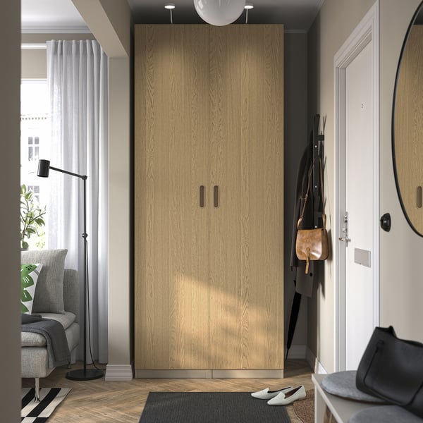 Modern entryway with tall wooden PAX wardrobe, coat rack, armchair, lamp, and striped rug.
