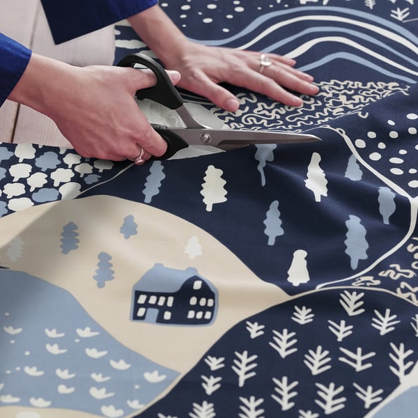 Person cuts colourful, patterned fabric with scissors.