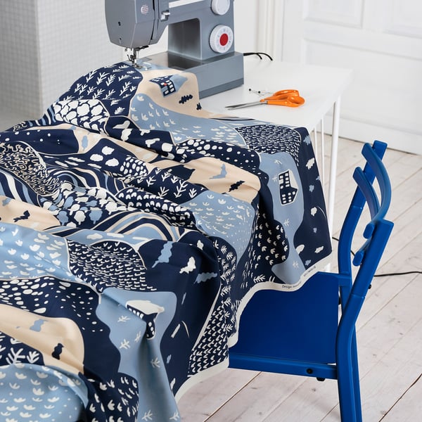 Blue chair beside table with sewing machine, colourful patterned fabric, scissors.