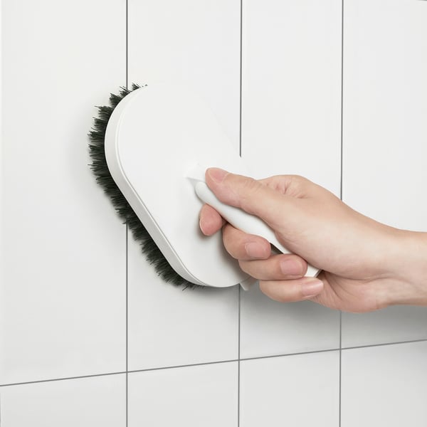 Person holding PEPPRIG brush, cleaning a tiled surface with it.
