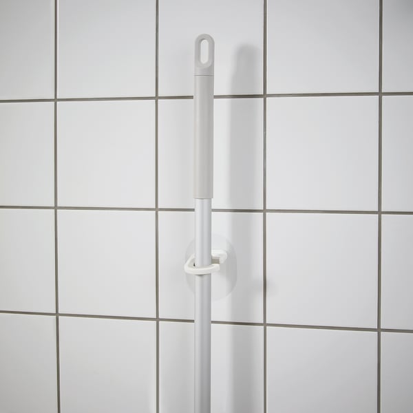 A white self-adhesive hanger mounted on a tiled wall, designed to hold cleaning tools without drilling holes.