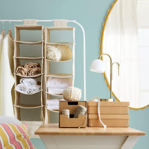 Small crafting desk with yarn, boxes, lamp, and hanging shelves.