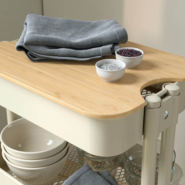 Wooden-topped trolley with stackable bowls, neatly folded grey cloths, sturdy cream legs, and baskets for storage.