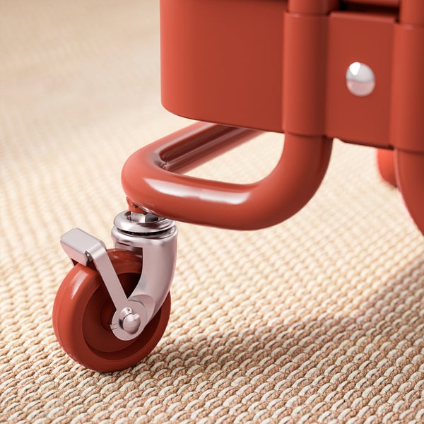 A close-up of a red, heavy-duty wheeled trolley on a beige carpet, showcasing its robust, lockable castor for stability.