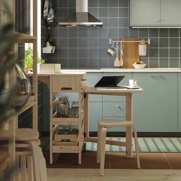 Wooden kitchen table with shelves, natural finish, blue cabinets, castors, and items on shelves, laptop on top.