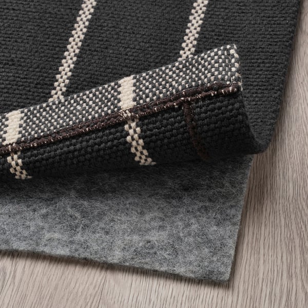 Grey cotton rug with off-white stripe, folded on wooden floor. Easy to clean and vacuum.