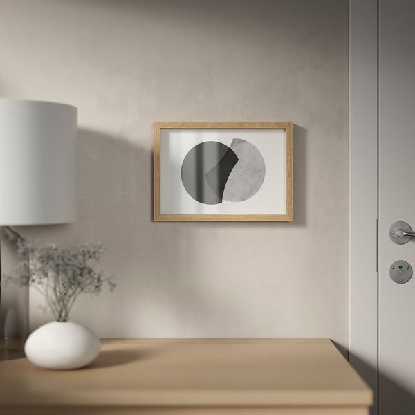 Framed abstract art hangs on wall above wooden table holding lamp and plant.