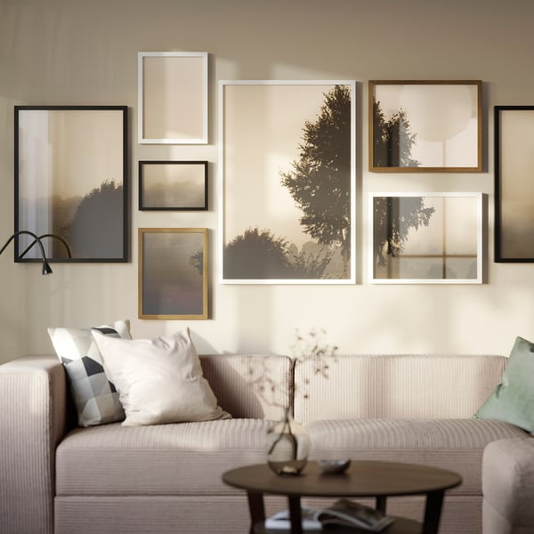 Beige RÖDALM frames show nature scenes on wall. Large light couch with decorative pillows and coffee table vase.