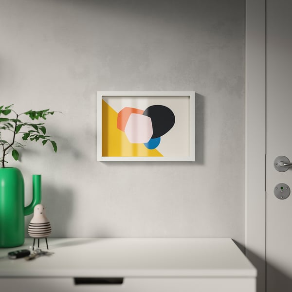 Abstract print in white frame on grey wall. Green vase with leaves, shapes, and keys below. Frame versatil.