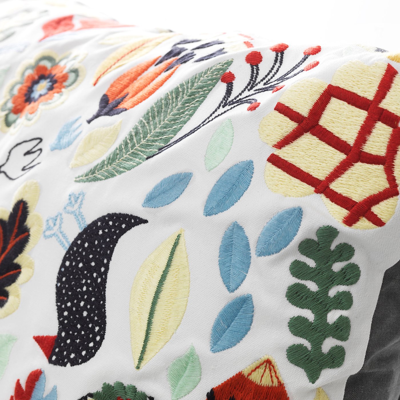 Colourful embroidered pillow with leaves, flowers, and geometric patterns on white base.