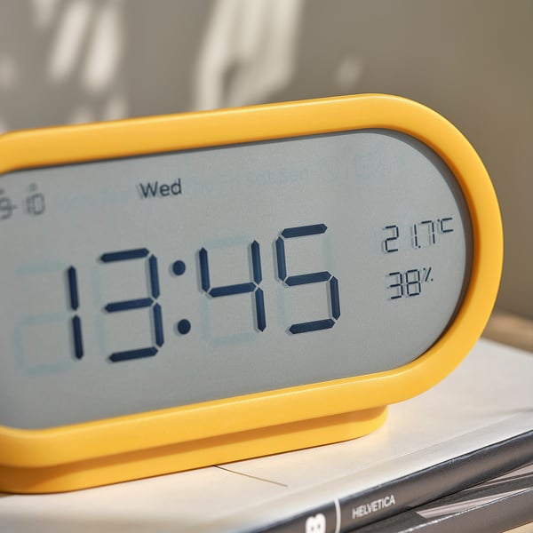 A bright yellow digital clock displaying 13:45, temperature 21. 7°c, humidity 38%, on a bedside table.