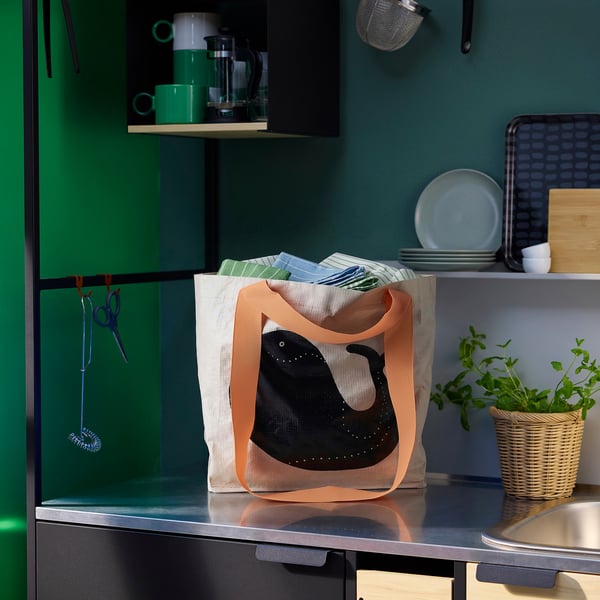 ROMELSÖN orange tote bag with black bird design on counter, smaller than green cups and larger than potted plant.