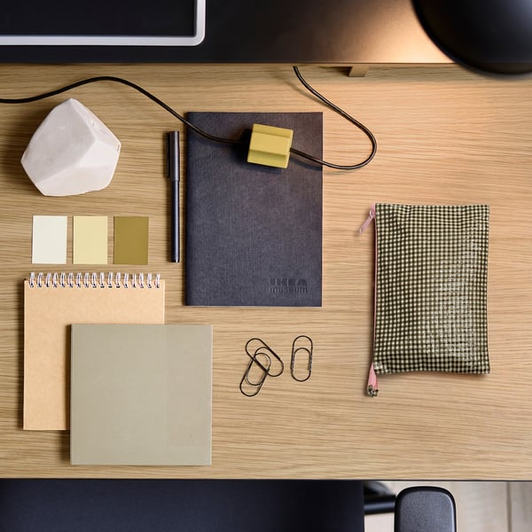 A wooden desk with ROMELSÖN black & white check bag, notebooks, paper clips, and accessories neatly arranged.
