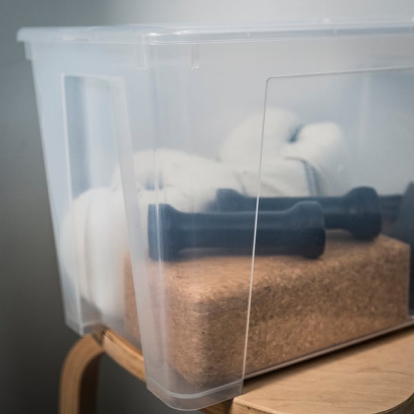 Clear plastic storage box, lid secured, containing black items on wooden surface.