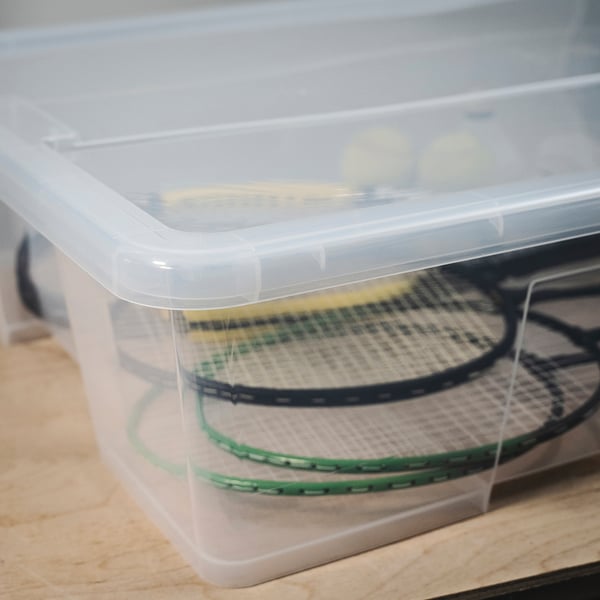 Clear plastic container with lid, holding two tennis rackets, showcasing its sturdy and transparent design.