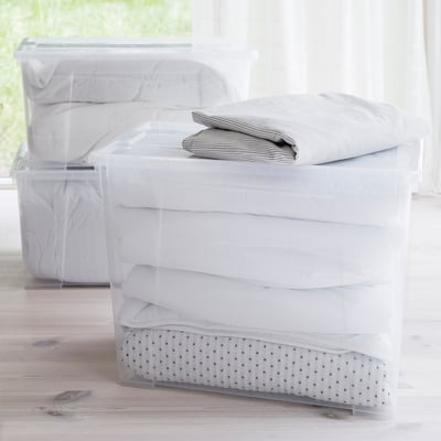 Clear plastic storage boxes stacked neatly, with folded linens inside, showcasing organisation and stackability.