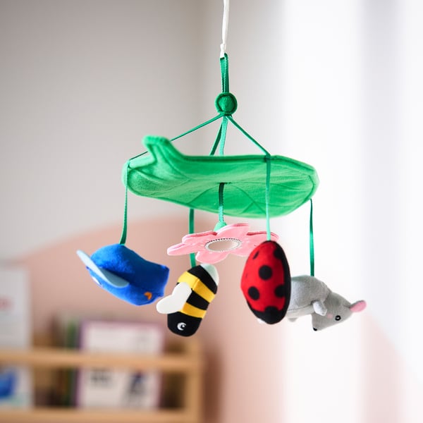 Colourful baby mobile with blue fish, bee, red ladybird, and grey mouse hanging from green leaf, stimulating vision and curiosity.