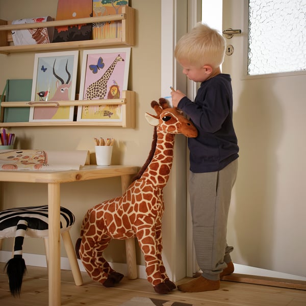 Boy brushes giraffe toy near art desk.
