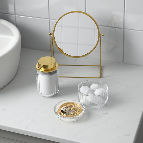 Marble counter with magnifying mirror, cotton jar, bracelets, and cotton bowl.