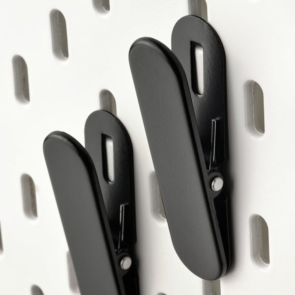 Black metal hooks on a white pegboard. Sturdy clips, arranged neatly, for organising items.