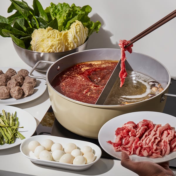 Hot pot setup with SKÄGGTORSK pot, showing different cooking compartments, non-stick surface, and various ingredients around it.