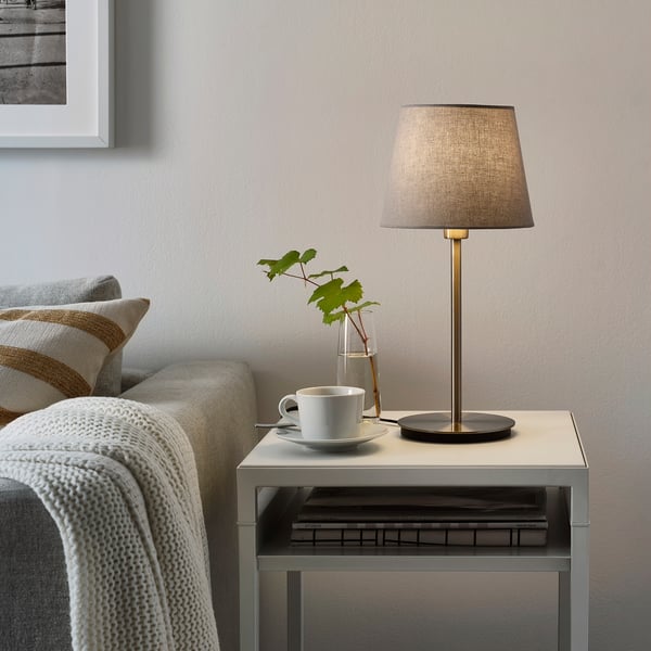 Small, modern table lamp, SKAFTET, grey, sleek design, fits beside couch with next to cup, vase, and books.