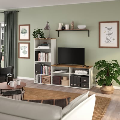 A cosy living room with a SKRUVBY tv stand, holding a tv, books, and decor. Light green walls, grey curtains, plants, and a coffee table with mugs.