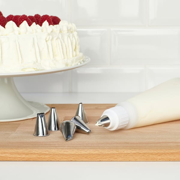 Silicone piping bag with metal tips on a wooden table, next to a frosted cake with berries on top.