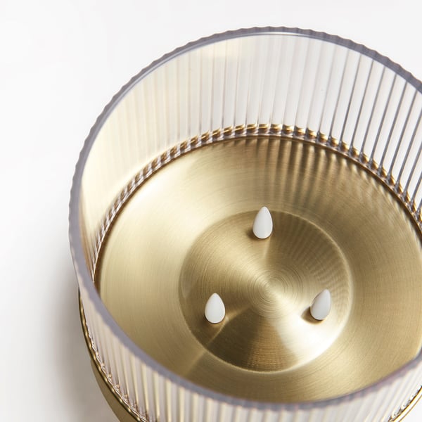 Gold-toned metal container with textured sides and three teardrop-shaped supports, holding a round base with a smooth finish.