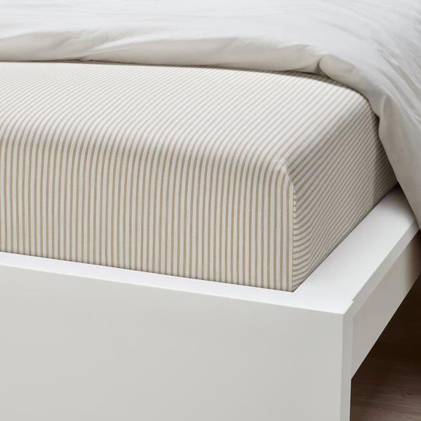 Neatly made bed with white and tan striped fitted sheet on a white frame.