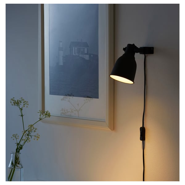 Wall-mounted black lamp illuminates a framed coastal art print next to a vase with flowers.