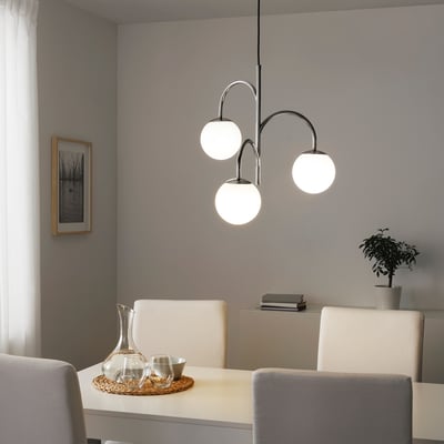 Modern dining area with sleek white furniture and a hanging light fixture featuring three transparent globes casting a soft, warm glow.