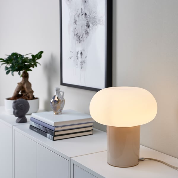 Beige lamp on desk with books, plant, near poster.
