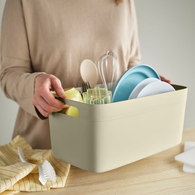 Person holding SPJUTLILJA dish drainer with plates and utensils.