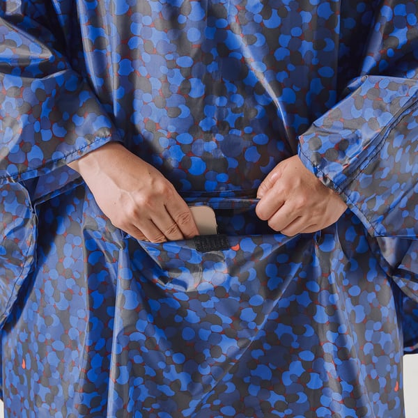 Person holding smartphone in pocket of patterned raincoat.