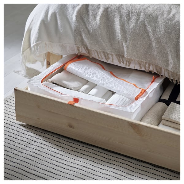 Bed with open drawer showing folded linens, white with orange border, on striped rug.