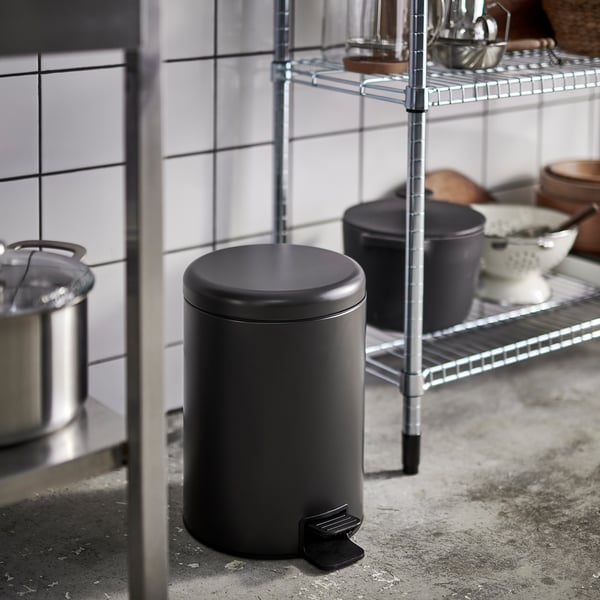 Small black pedestal bin in kitchen with wire shelves, pots, and bowls.