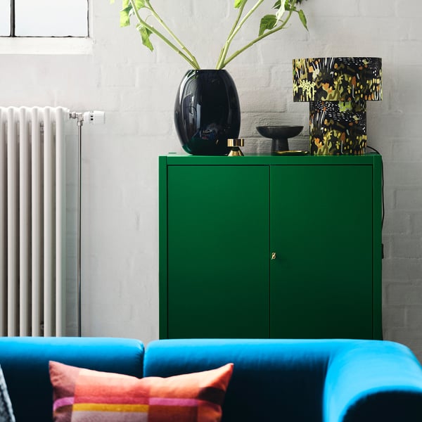Bright living room with vibrant blue couch, colourful pillow, green cabinet, and a tall decorative lamp with foliage design on top.