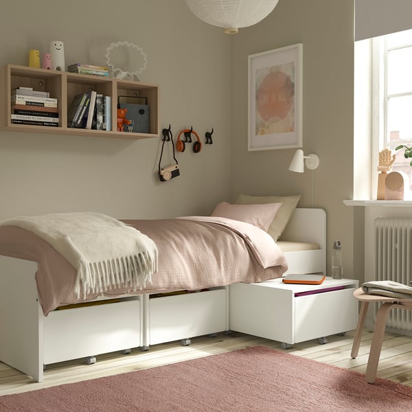 Cosy bedroom with pale pink STOENSE rug, low-pile bed, white drawers, wooden table, and bookshelf with magic poster.