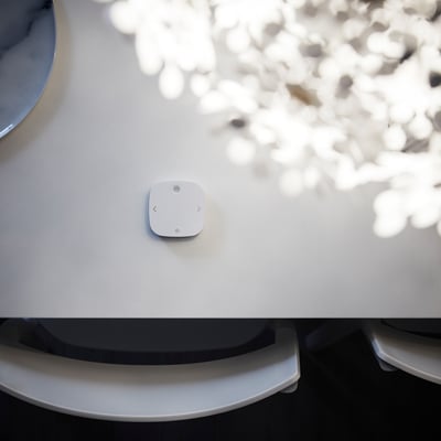 Small white rectangular remote control on a white surface, surrounded by light patterns.