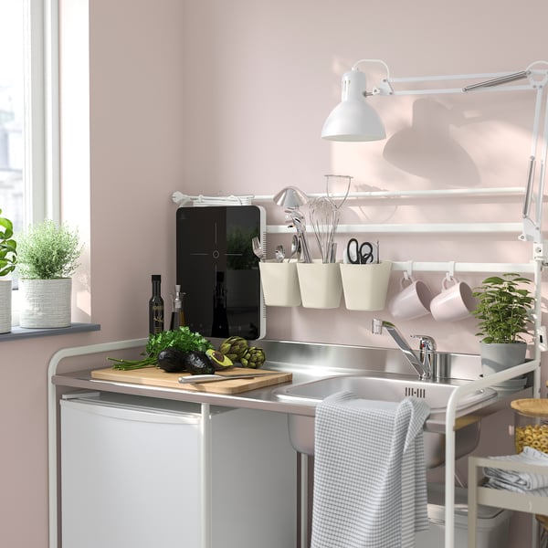 Small white SUNNERSTA kitchen organiser holding utensils, hanging cups, and plants beside sink.