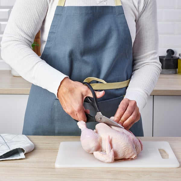 Person uses scissors to prepare chicken on cutting board in kitchen.