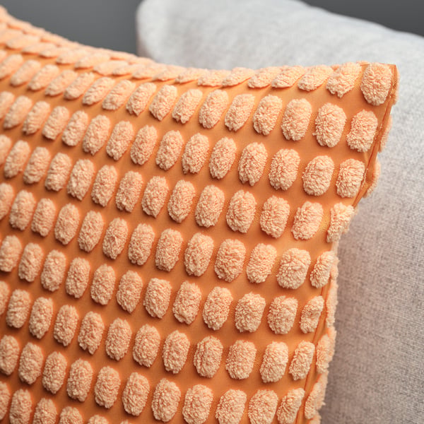Close-up of an orange cushion with a soft, textured pattern on a bed.