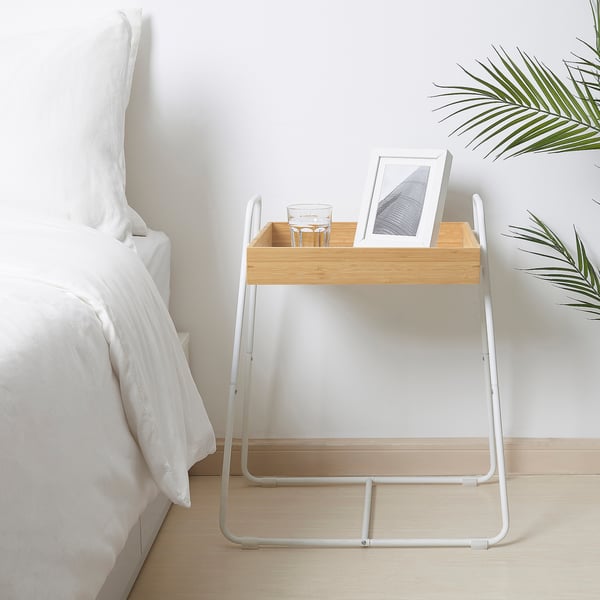 Bamboo tray side table with white metal frame, beside bed, holds glass & picture.