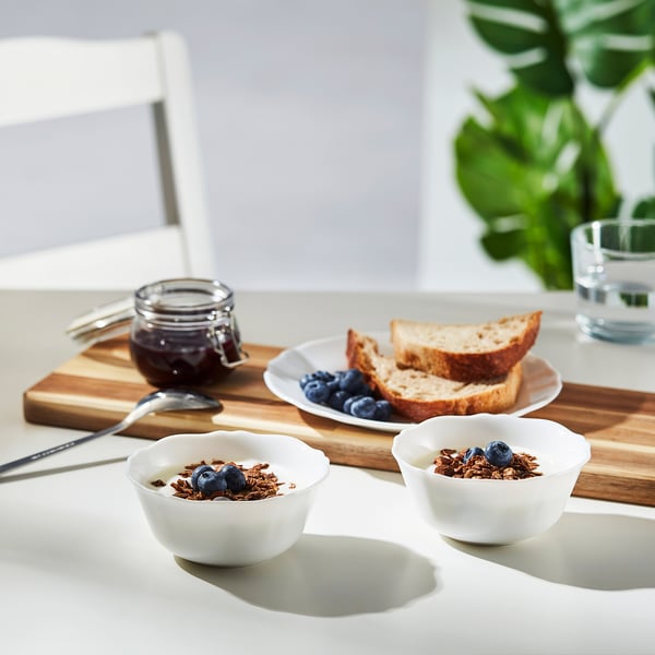 Two bowls of yoghurt with granola and blueberries on a wooden board with toast, berries, and jam.