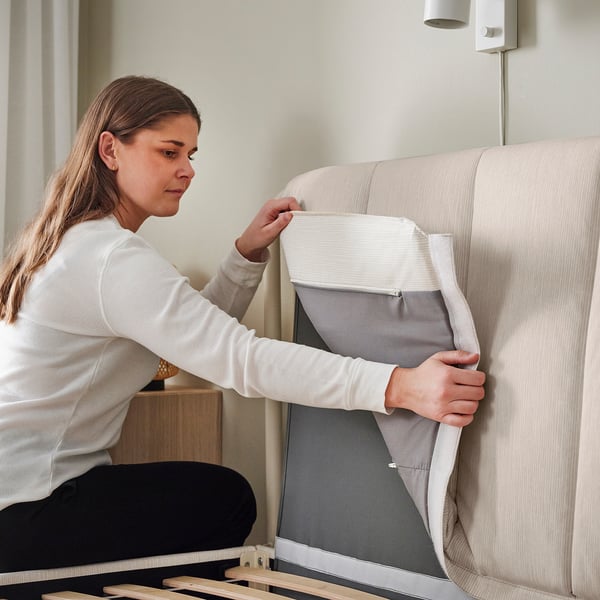 A person attaches a light beige, striped upholstered headboard to a bed frame, showcasing the easy assembly and modern design.