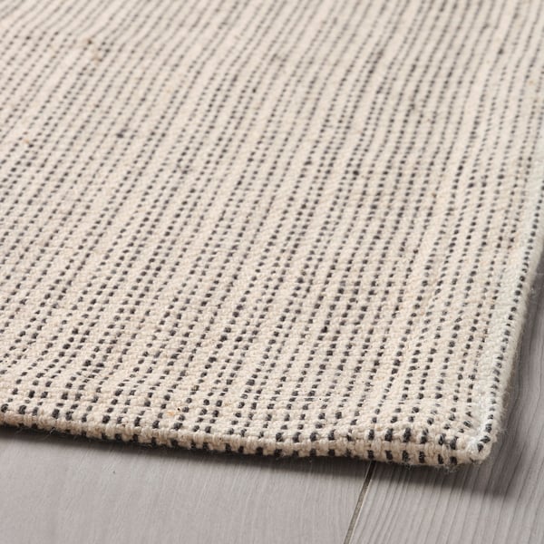 Beige and grey woven cotton rug with intricate diagonal stripes, laid on a wooden floor.